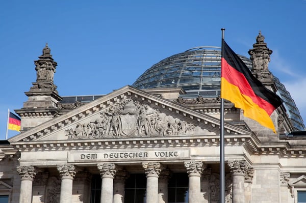 Reichstagsgebäude in Berlin mit Glaskuppel und deutscher Flagge vor blauem Himmel