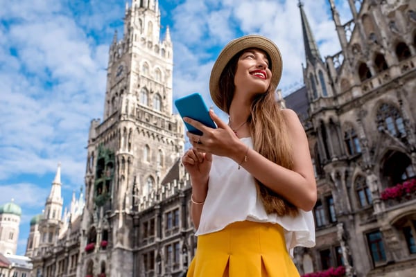 Touristin mit Smartphone auf dem Marienplatz in München vor dem Neuen Rathaus und blauem Himmel