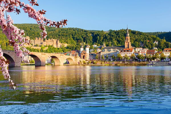 Blick auf Heidelberg mit Alter Brücke, Altstadt und Schloss vor bewaldeten Hügeln im Frühling