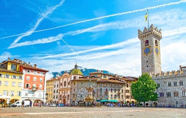 Historischer Marktplatz mit steinernem Uhrturm, Brunnen und bunten Gebäuden vor blauem Himmel