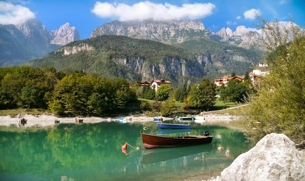 Ruhiger Bergsee mit kleinen Booten, grünen Ufern und imposanten Felsbergen im Hintergrund