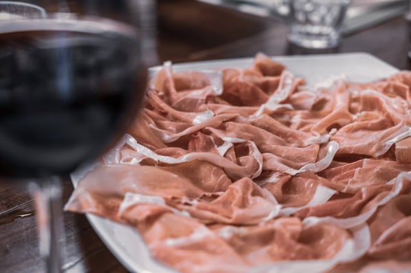 Dünn geschnittener Schinken auf weissem Teller mit Glas Rotwein im Vordergrund