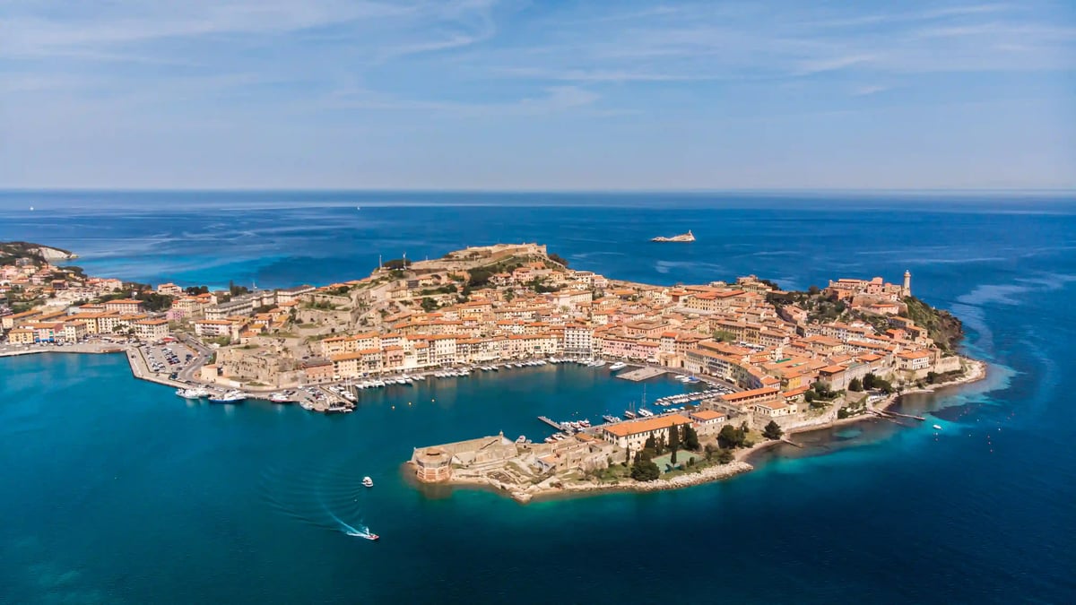 Luftaufnahme einer grossen Bucht mit Hafenstadt, vielen Booten und türkisfarbenem Wasser, umgeben von Küste und offenem Meer.