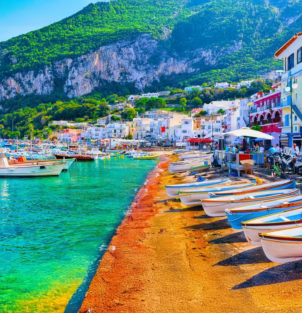 Bunter Hafenort auf Capri mit kleinen Booten, Häusern am Wasser und steilen grünen Berghängen