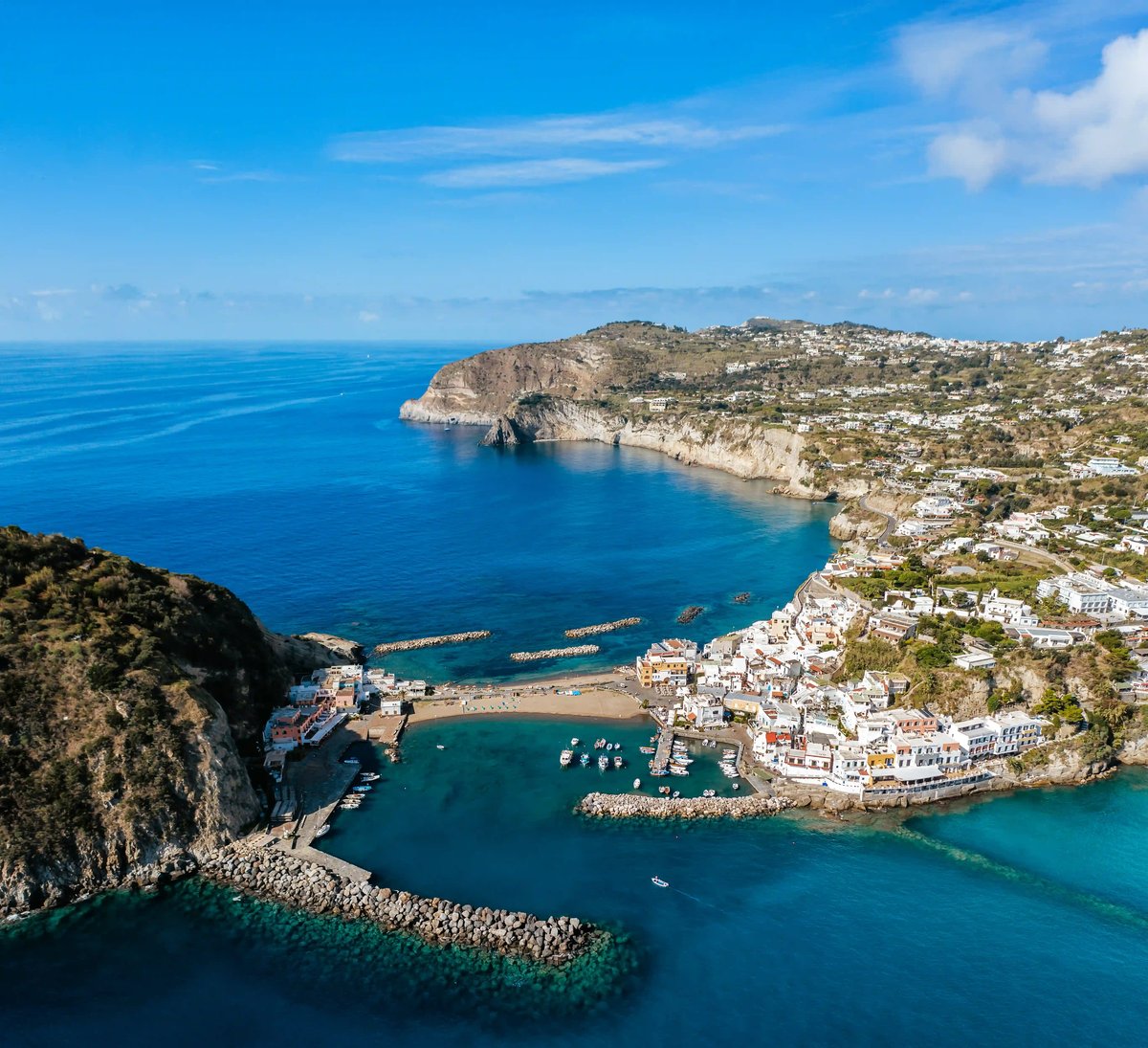 Village côtier de Sant Angelo sur Ischia avec maisons blanches, port, eau turquoise et falaises rocheuses