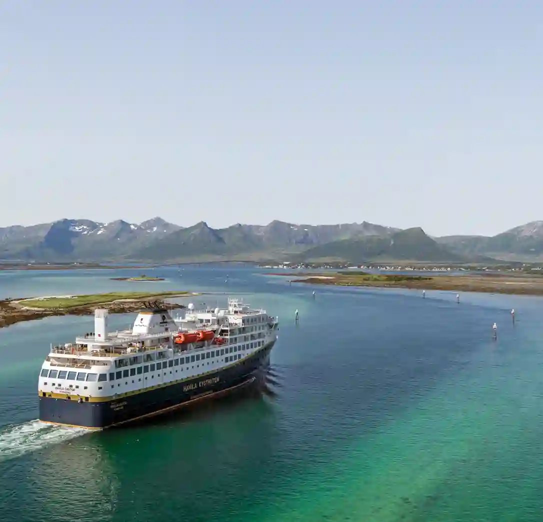 Navire côtier Havila navigue sur une mer turquoise devant des montagnes et des îles