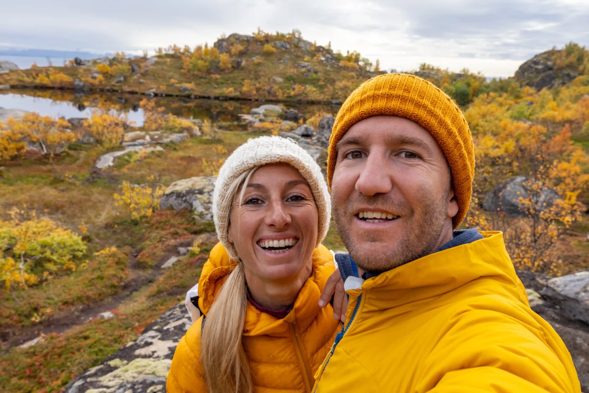 Couple souriant en vestes jaunes prend un selfie dans un paysage d'automne avec lac et rochers