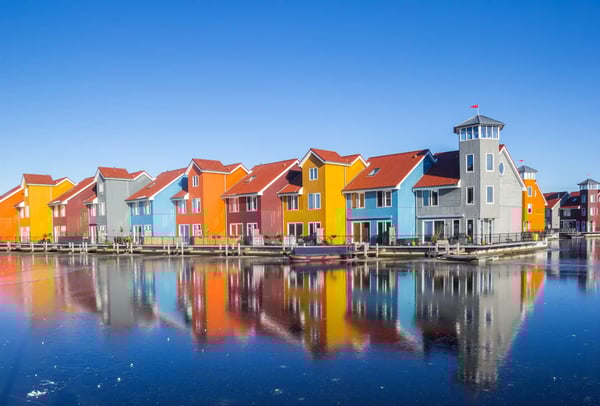 Bunte moderne Häuser mit roten Dächern spiegeln sich im ruhigen Wasser einer Wohnsiedlung in den Niederlanden