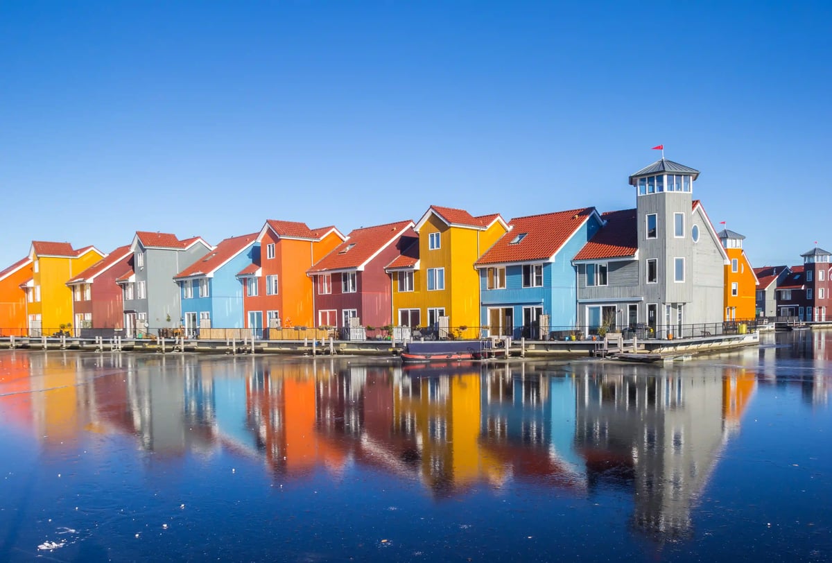Bunte moderne Häuser mit roten Dächern spiegeln sich im ruhigen Wasser einer Wohnsiedlung in den Niederlanden