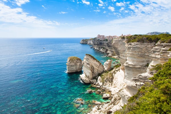 Weisse Kalkfelsen an der Küste bei Bonifacio mit türkisfarbenem Meer und Blick auf die Stadt auf der Klippe im Hintergrund