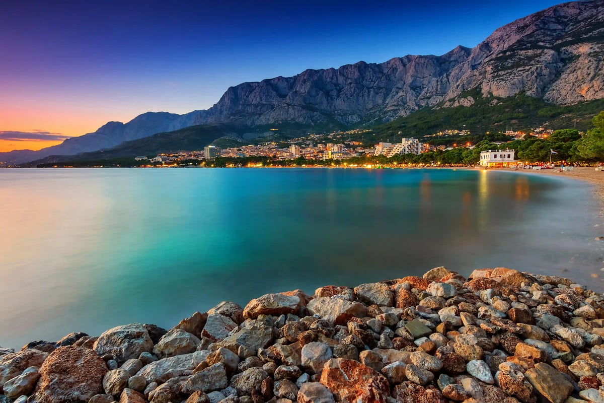 Paysage côtier de la Riviera de Makarska en soirée avec ville éclairée, mer calme et hautes montagnes