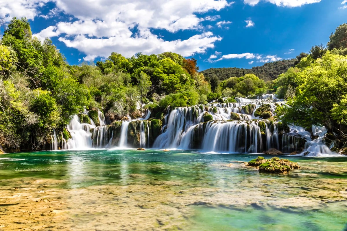 Cascades larges du parc national de Krka avec eau claire, végétation verte et lit de rivière peu profond