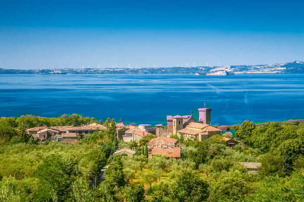 Vue sur le lac de Bolsena d'un bleu intense avec un village médiéval au premier plan entouré de collines verdoyantes