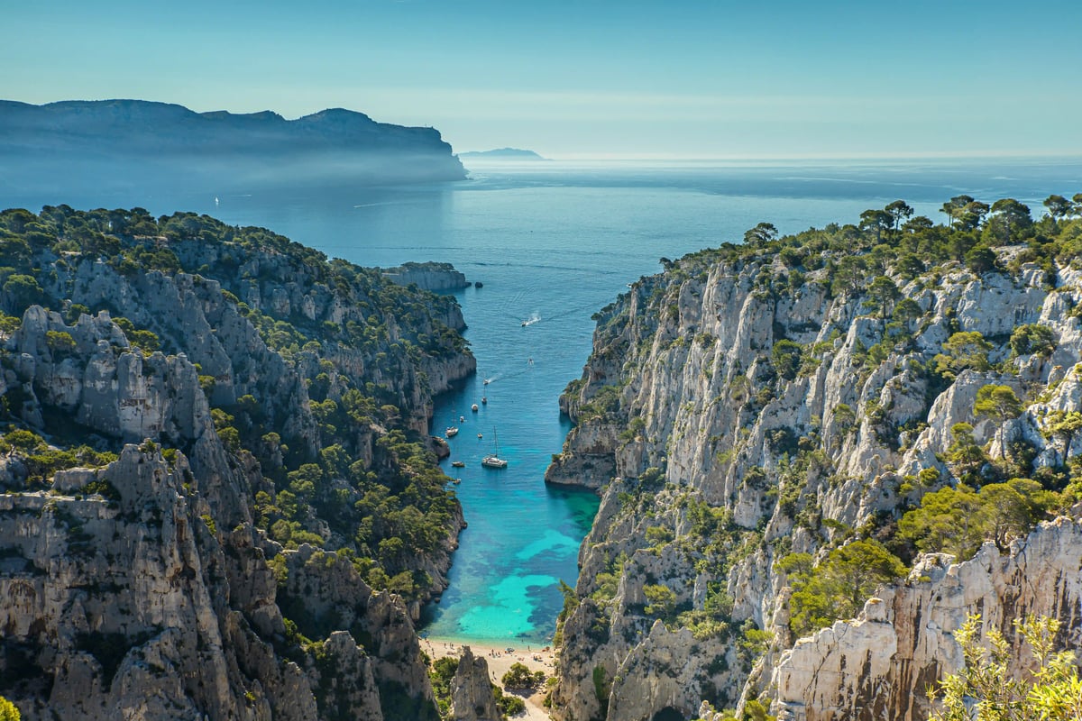 Türkisfarbene Bucht zwischen steilen Kalkfelsen der Calanques mit Booten und Mittelmeer im Hintergrund