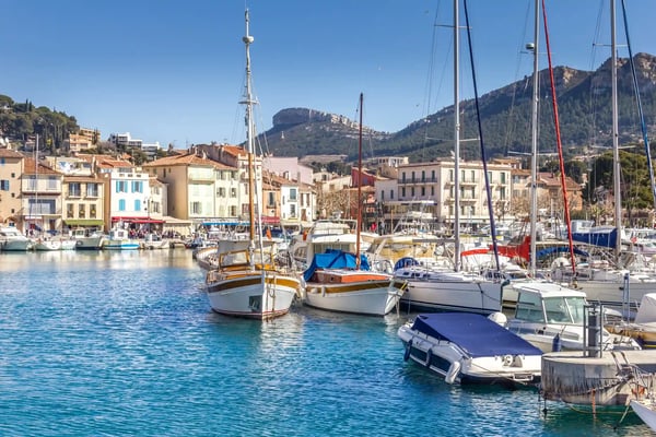 Hafen von Cassis mit Segelbooten, bunten Häusern am Wasser und Bergen im Hintergrund