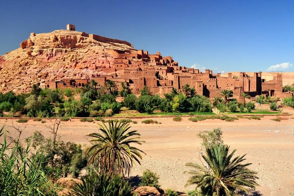 Lehmburg Aït Benhaddou auf Hügelkamm, terrassierte Häuser über Palmen und trockenem Flusstal.