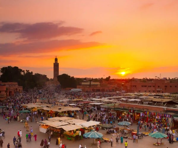 Belebter Djemaa el-Fna in Marrakesch bei Sonnenuntergang, Marktstände und viele Menschen vor dem Minarett.