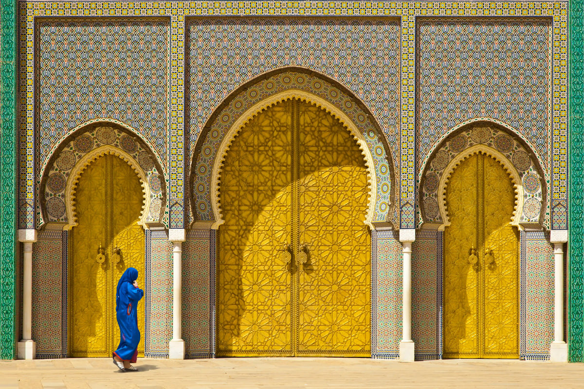 Reich verzierte goldene Tore mit Mosaikrahmen in Fès, Person im blauen Gewand läuft davor vorbei.