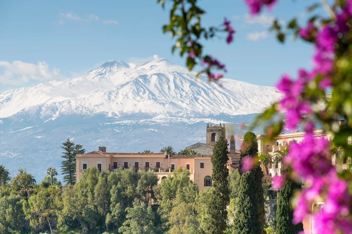 Volcan Etna enneigé dominant une ville sicilienne avec bâtiments historiques et jardins