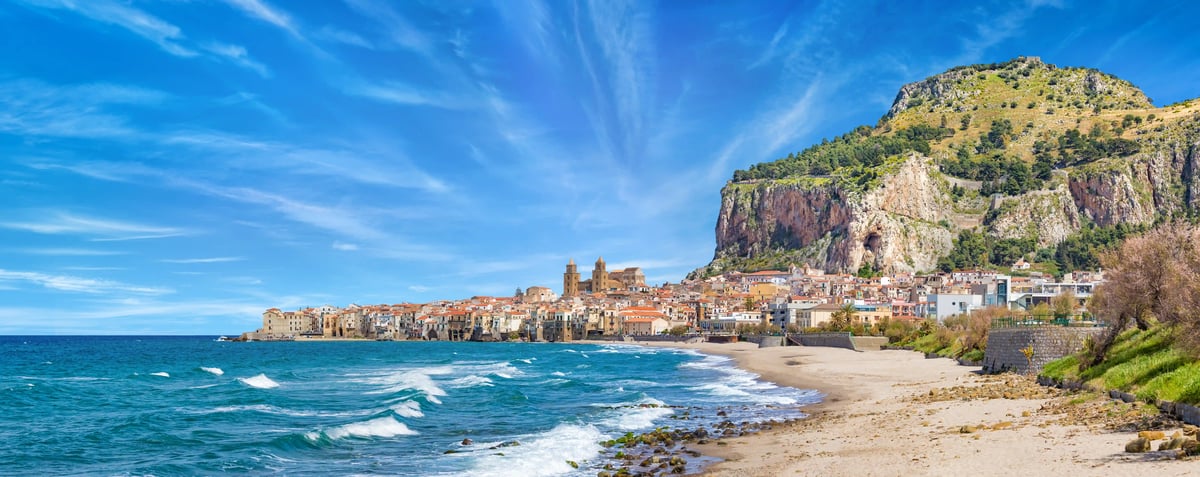 Küstenstadt Cefalu mit Sandstrand, blauem Meer und Altstadt vor einem steilen Felsen