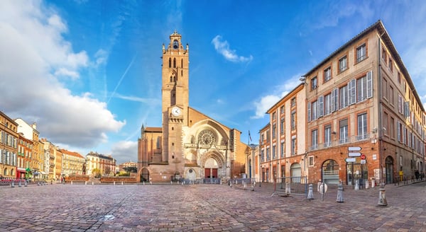 Grosser Platz in Toulouse mit Kathedrale, Glockenturm und historischen Backsteingebäuden unter blauem Himmel.