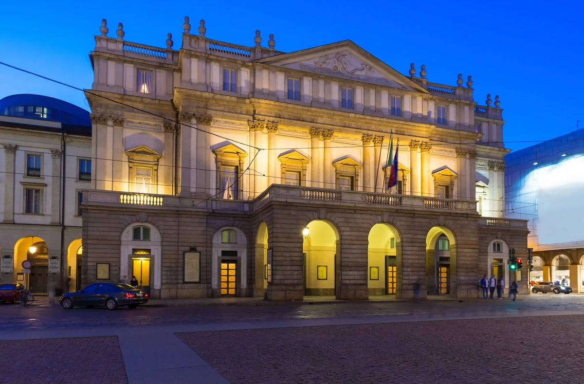 Façade illuminée du Teatro alla Scala à Milan en soirée avec arcades et place devant le bâtiment