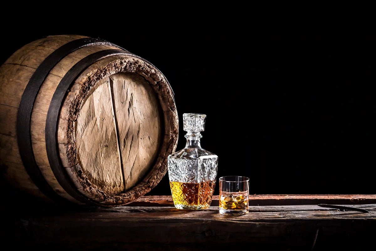 Holzfass mit gefüllter Whisky Karaffe und Glas auf rustikalem Tisch vor dunklem Hintergrund