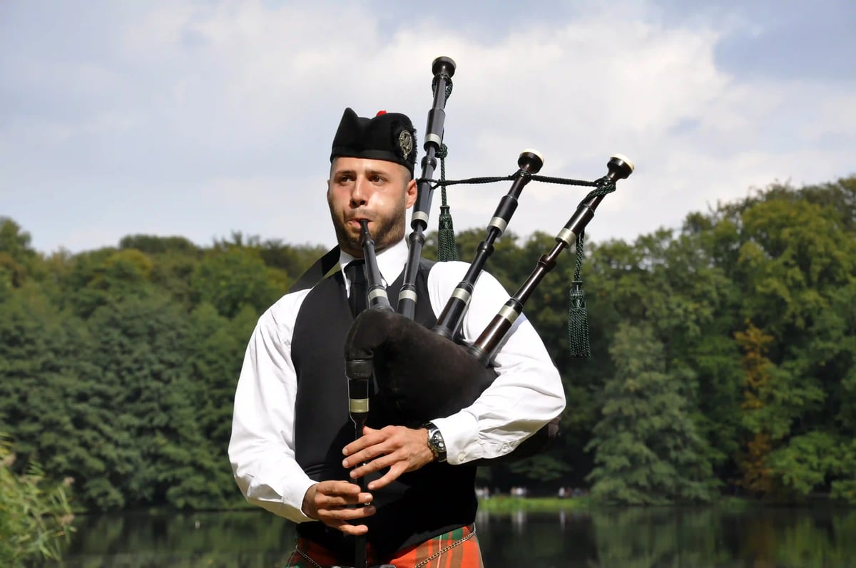 Dudelsackspieler in traditioneller schottischer Kleidung spielt im Freien vor grüner Landschaft