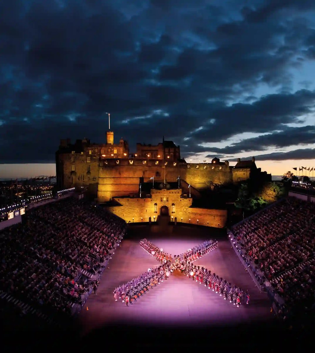 Edinburgh Castle bei Nacht mit beleuchtetem Vorplatz und militärischer Musikformation vor Publikum