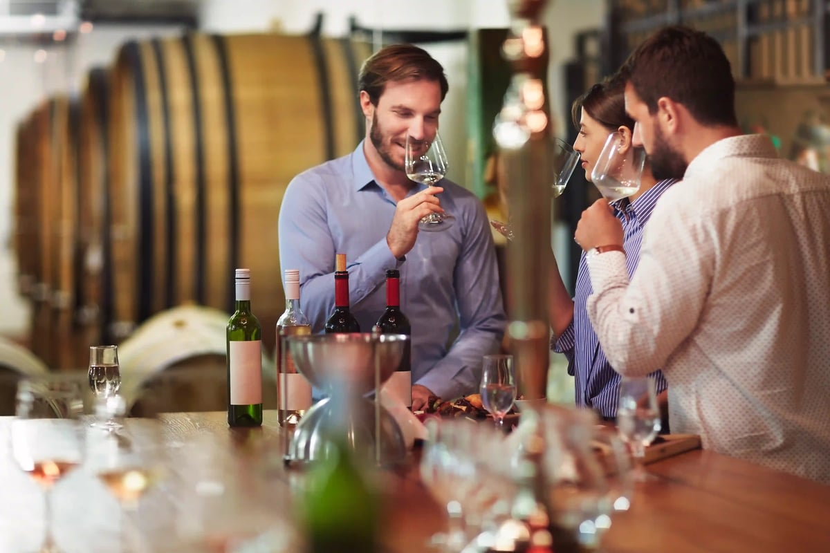 Gruppe von Personen bei einer Weinprobe im Weinkeller mit Holzfässern und Weingläsern