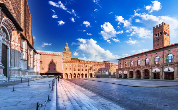 Weite Piazza in Bologna mit historischen Backsteinbauten und Arkaden bei klarem Himmel