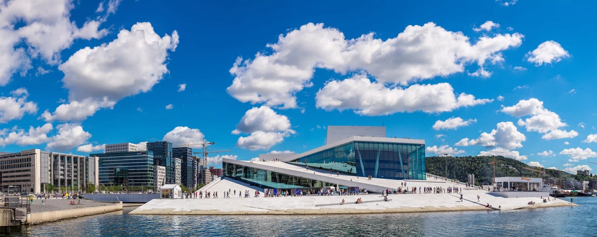 Weisse, schräge Dachflächen der Oper in Oslo am Hafen, Menschen spazieren auf dem Dach, blauer Himmel mit Wolken.