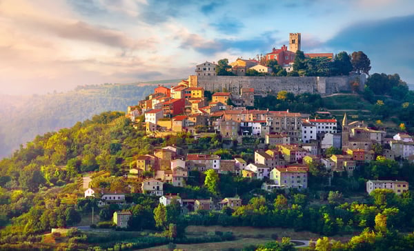 Historisches Bergdorf mit Natursteinhäusern und Burg auf einem Hügel in grüner Landschaft