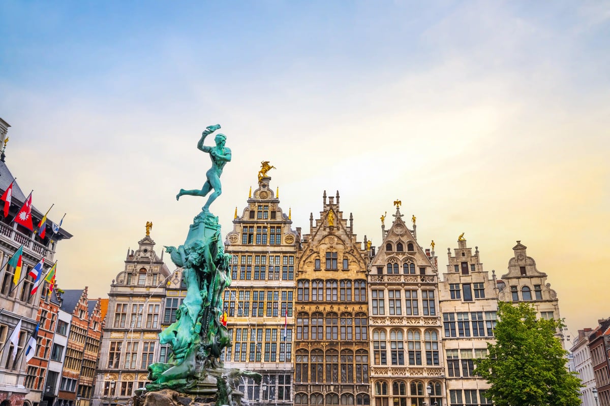 Fontaine de Brabo avec statue devant les maisons de guildes ornées de la Grand-Place d'Anvers, sous une lumière dorée
