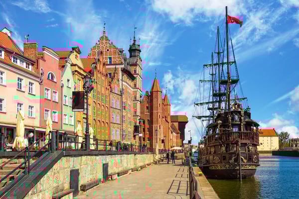 Bunte historische Giebelhäuser an der Uferpromenade der Altstadt von Danzig mit einem festgemachten historischen Segelschiff bei blauem Himmel
