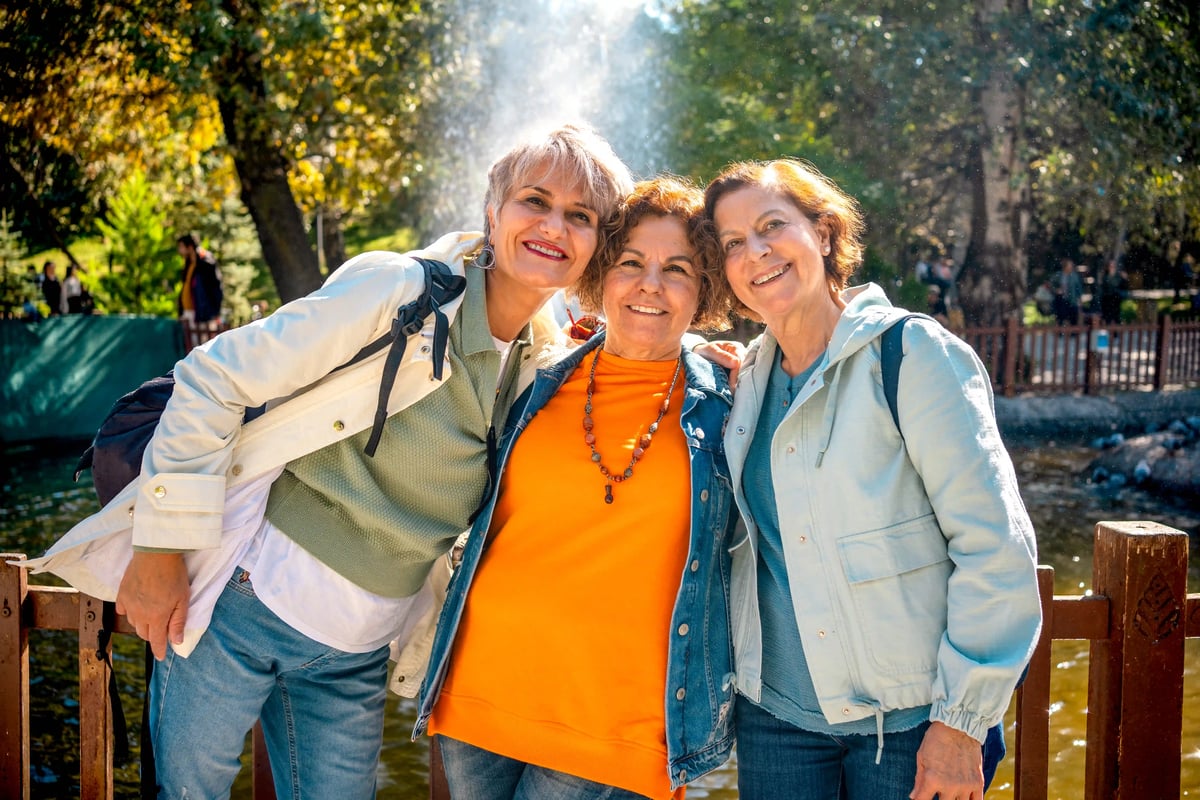 Trois femmes souriantes se tiennent cote a cote en plein air et profitent ensemble d'une excursion dans la nature