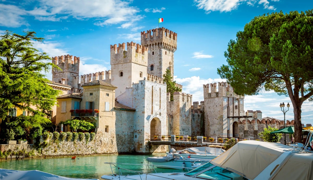 Le chateau Scaliger de Sirmione avec douves, bateaux et remparts historiques sous un ciel ensoleille