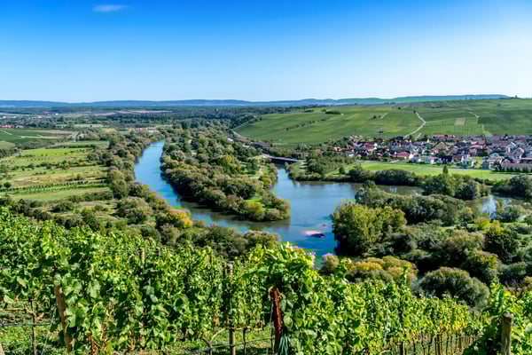 Flusslandschaft mit Weinbergen, grünen Hügeln und Dorf im Hintergrund bei klarem Wetter