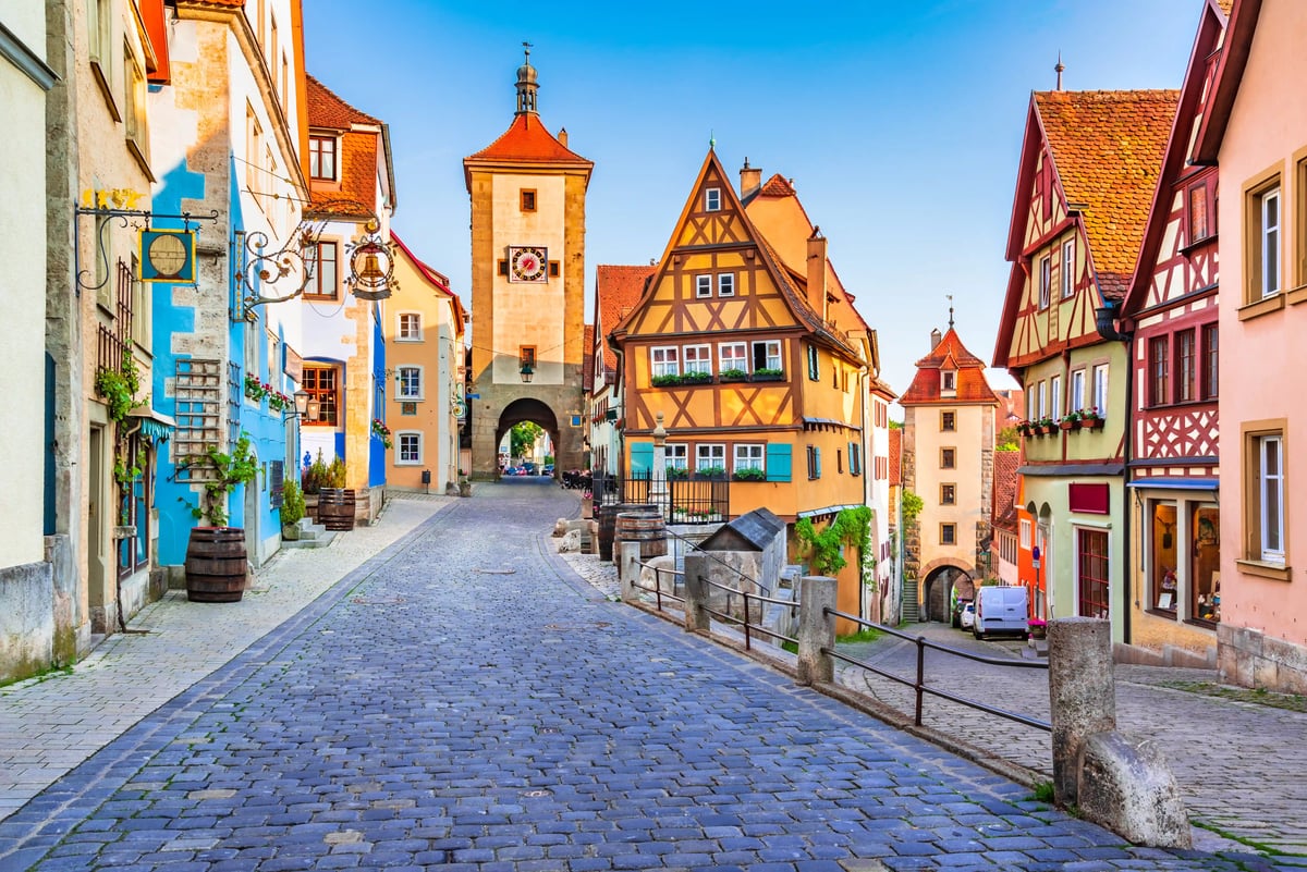 Kopfsteingasse in Rothenburg ob der Tauber mit farbigen Fachwerkhäusern, Stadttor und blauem Himmel