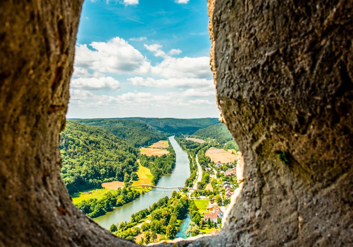 Blick durch eine Felsöffnung auf das grüne Altmühltal mit Fluss, Wiesen und bewaldeten Hügeln
