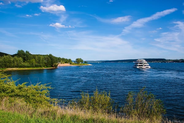 Ausflugsschiff fährt über den blauen Brombachsee mit Uferlandschaft, Bäumen und weitem Himmel