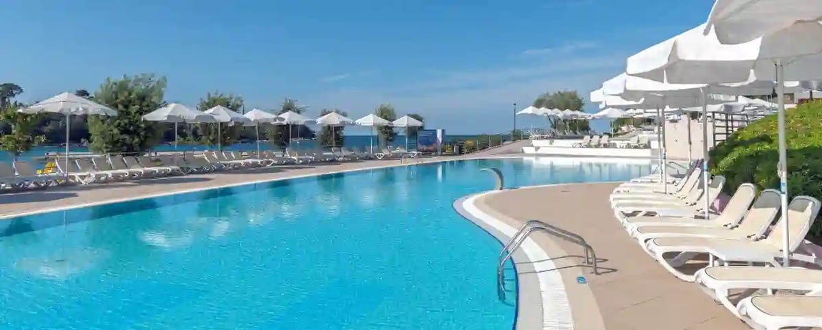Grosse Hotel Poolanlage mit Liegen und Sonnenschirmen unter blauem Himmel
