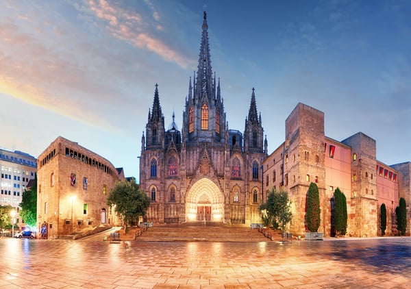 Beleuchtete Sagrada Família in Barcelona bei Abenddämmerung mit gotischer Fassade und gepflastertem Platz im Vordergrund