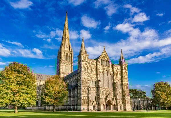 Gotische Kathedrale von Salisbury mit hohem Turm auf weiter Grünfläche unter blauem Himmel