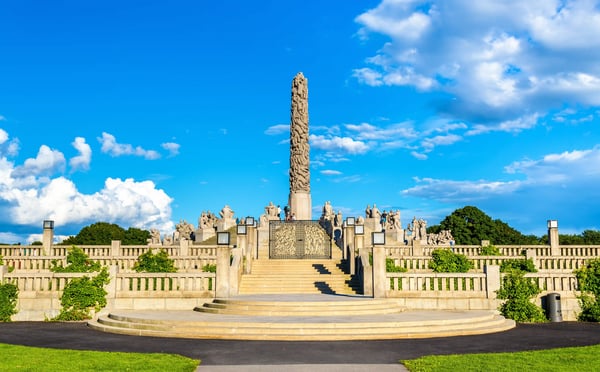 Vigeland-Skulpturenpark in Oslo mit hoher Monolith-Säule, Treppenanlage und Figuren unter blauem Himmel