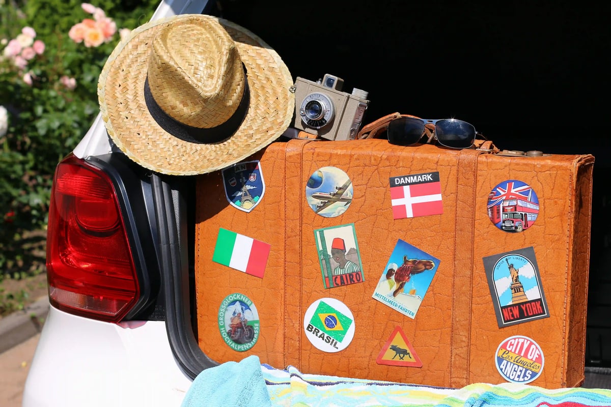 Alter Reisekoffer mit Aufklebern aus aller Welt und Strohhut im Kofferraum