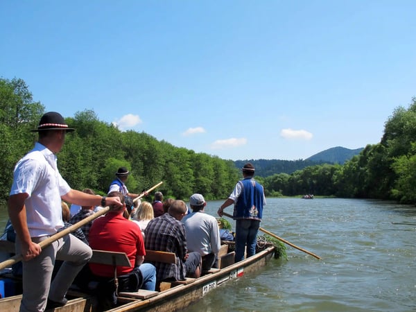 Gruppe von Menschen fährt auf einem Holzfloss durch einen Fluss mit bewaldeten Ufern