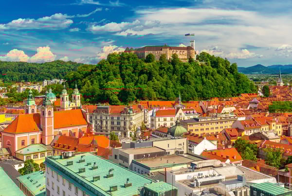 Blick über die Altstadt von Ljubljana mit barocken Gebäuden, roten Dächern und der Burg auf bewaldetem Hügel