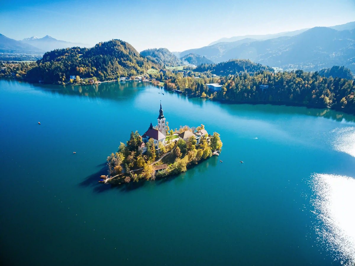 Luftaufnahme der Marieninsel mit Kirche im Bleder See, umgeben von türkisfarbenem Wasser und bewaldeten Hügeln