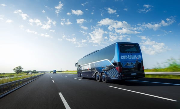Moderner Reisebus fährt auf einer freien Autobahn durch eine flache Landschaft unter blauem Himmel mit weissen Wolken